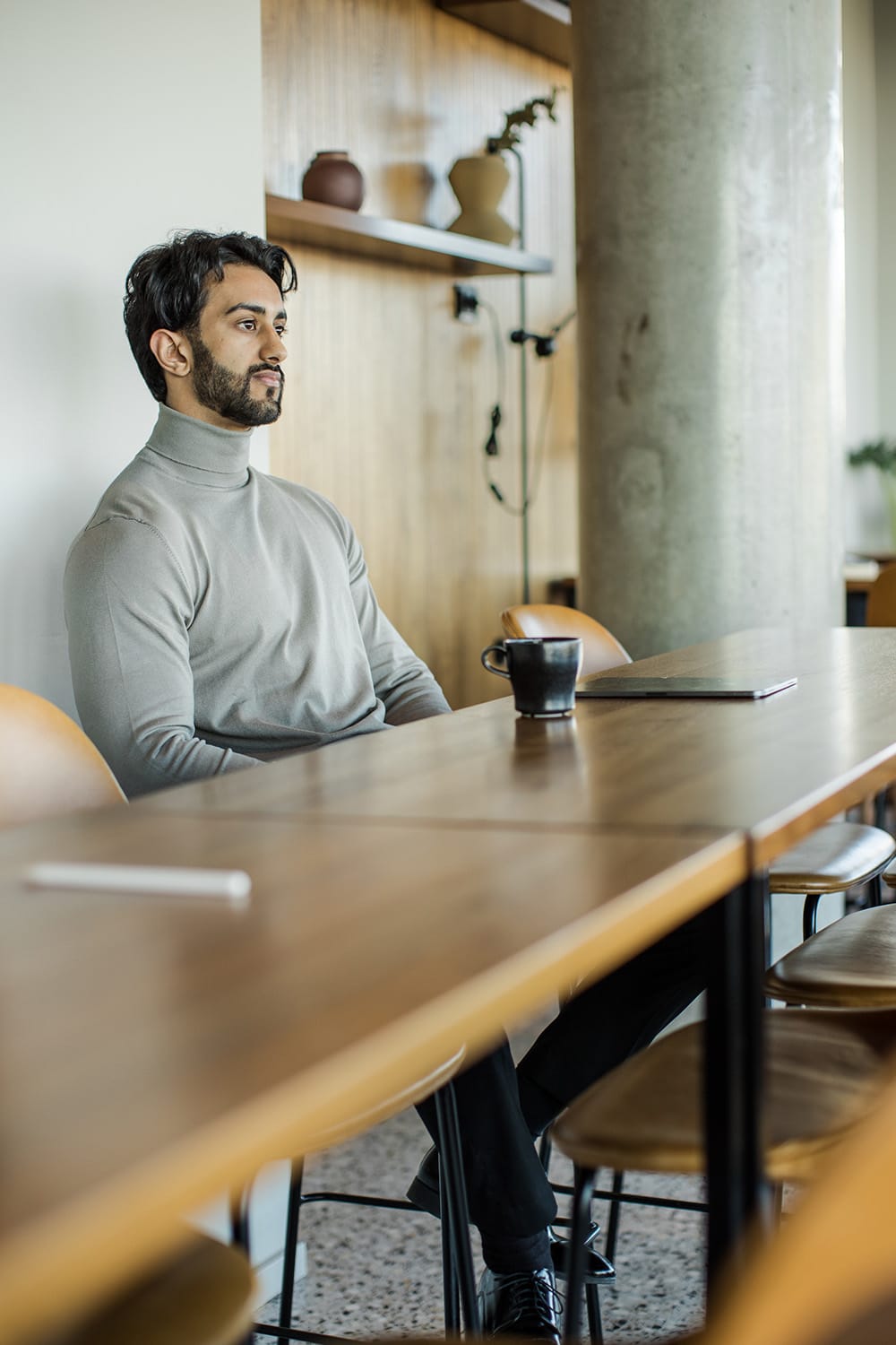 Liten bedrifts-eier, mann som sitter på kafé, lene seg tankefullt med en kopp te, reflekterende på en profesjonell men avslappet måte