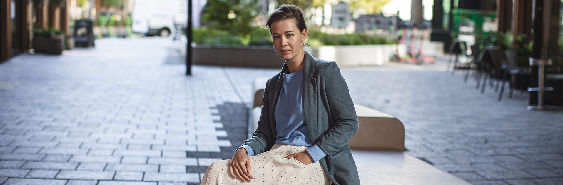 Profesjonelt bilde av en kvinne i business casual antrekk som sitter i et urbant miljø, med en vennlig og imøtekommende utstråling, perfekt for markedsføring og merkevarebygging på nettsider.
